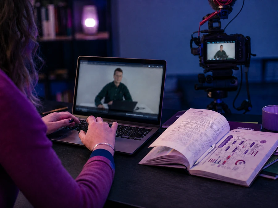 Médica assistindo a uma aula da plataforma HORMOFEM no notebook, com o livro aberto ao lado
